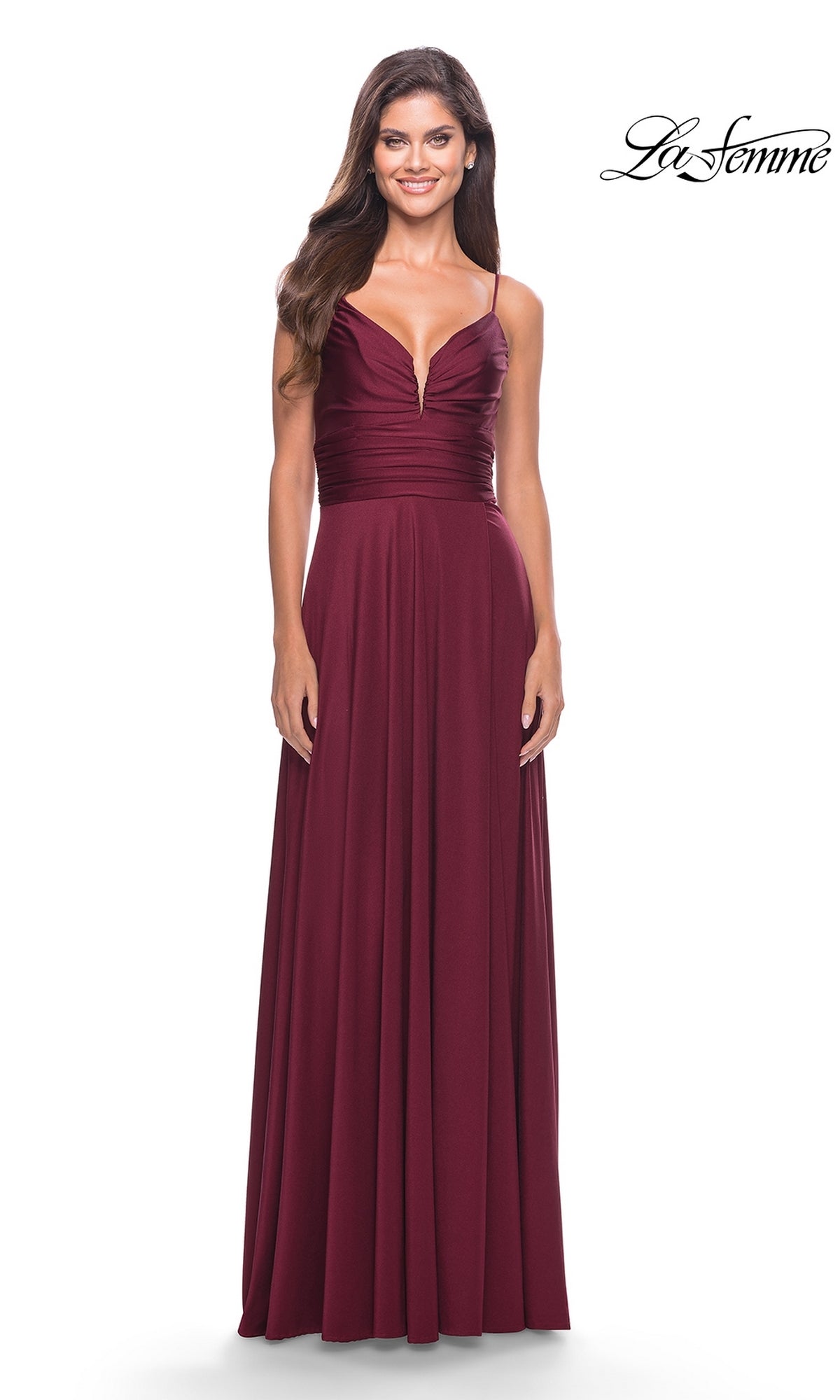 A woman wears the La Femme Simple Long A-Line Prom Dress 31090, featuring a sleeveless, floor-length burgundy design with a deep V-neckline, ruched bodice, and spaghetti straps. The